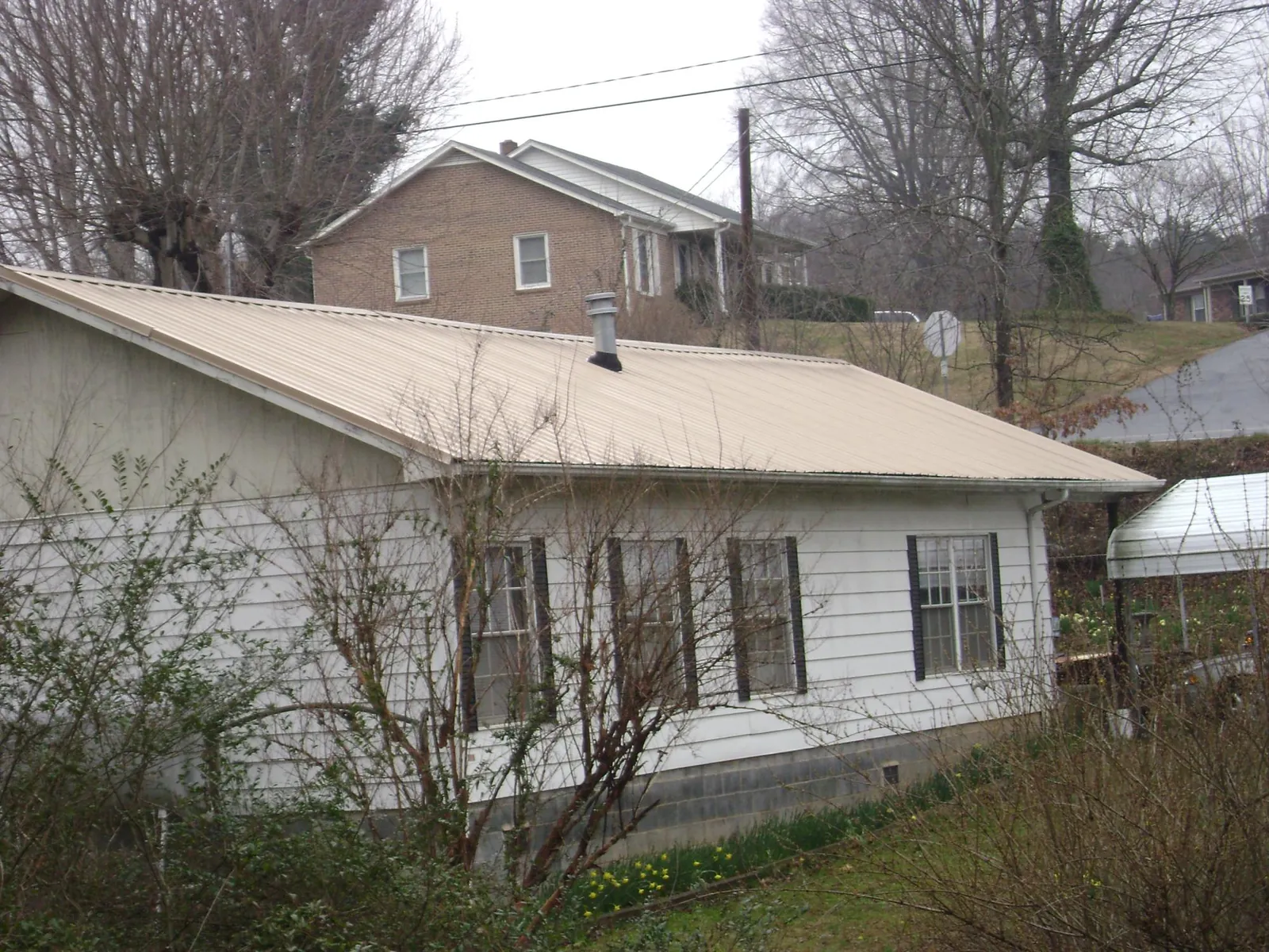 Tan metal roof on a white sided house set into a hillside — Commercial Roofing by Roofing Brothers in Vero Beach